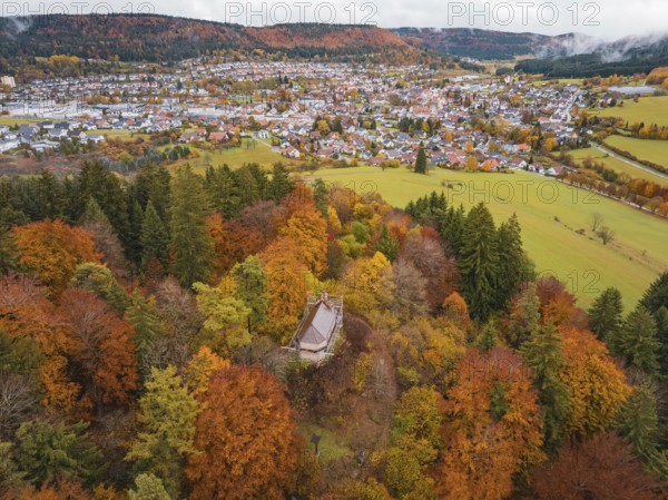 Pavilion in the middle of a colorful autumn forest with a view of a distant city and hills under