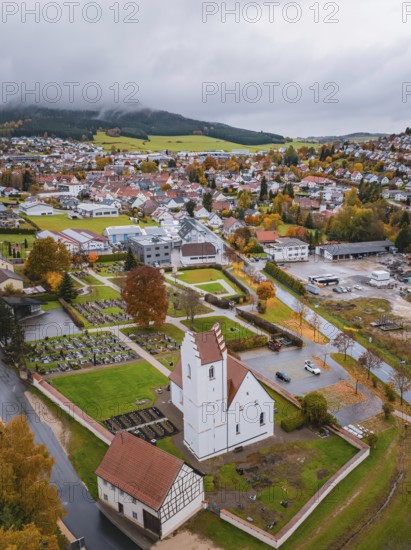 View of a town with church and cemetery surrounded by autumn trees and residential buildings on a