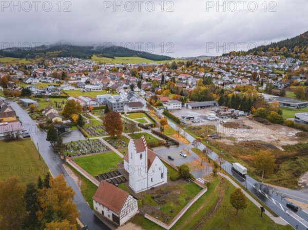 Urban view with church and residential buildings surrounded by autumn trees and mountains under a