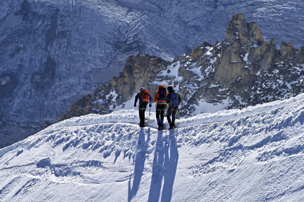 Three ascended mountaineers run across a snow-covered mountain ridge, Aiguille du Midi,