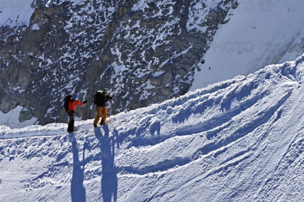 Two mountaineers run across a snow-covered mountain ridge, Aiguille du Midi, Chamonix-Mont-Blanc,