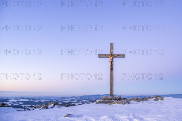 Christian cross on the peak of Mount Lusen with the view over the hills of the bavarian forest at