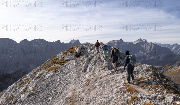 Hikers on the summit ridge of the Gamsjoch, behind rock faces of the Laliderer Spitze, eastern