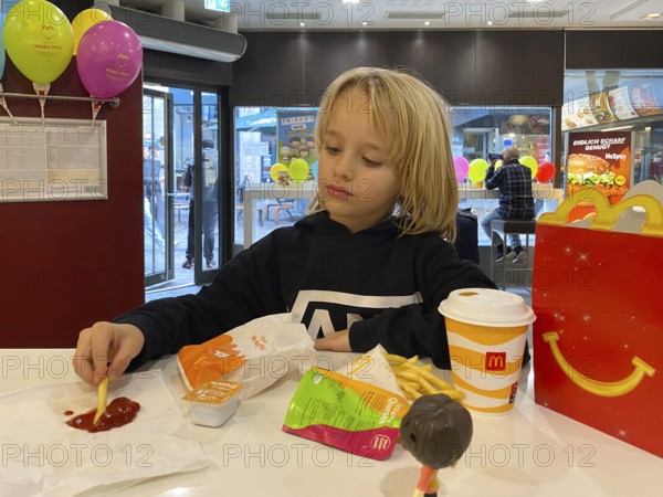 Interior view, child, boy, 7 years, blonde, eating Happy Meal, children's menu, at McDonald's