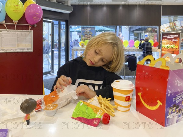 Interior view, child, boy, 7 years, blonde, eating Happy Meal, children's menu, at McDonald's