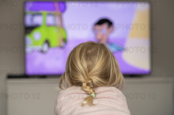 Child, girl, 4 years old, blonde, lying on sofa, watching TV, watching television, in front of