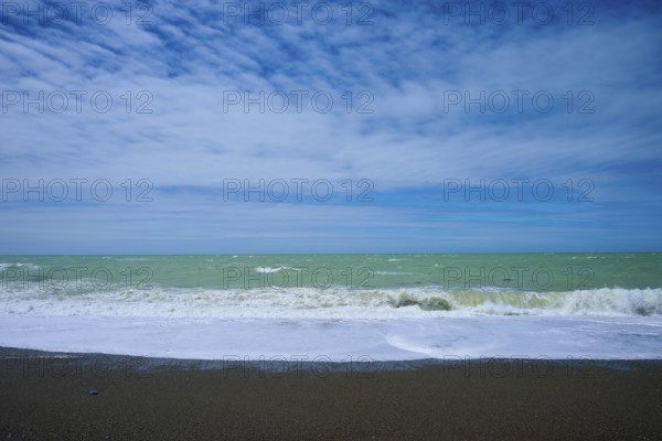 Wavy beach with calm sky in the background, Tuhawaiki Point Lighthouse or Jack's Point Lighthouse,