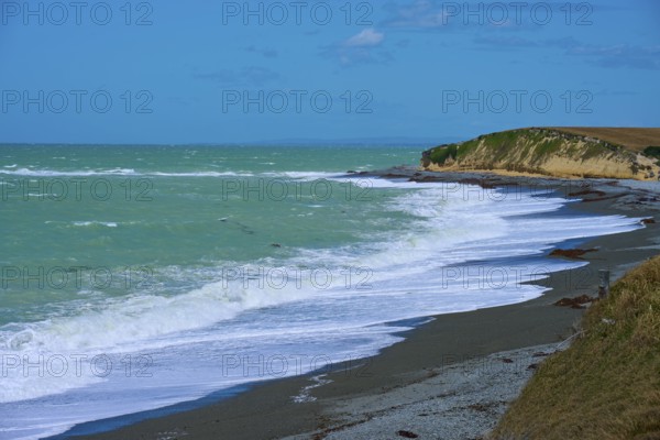Waves crash against a rocky coast with blue sky, Tuhawaiki Point Lighthouse or Jack's Point