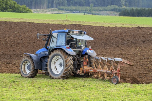 Tractor with plough, agricultural ploughing machine working on a field in autumn, fall in the
