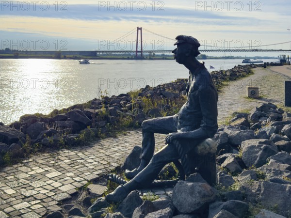 Photo with melancholy mood of bronze sculpture Poortekerl looking at Rhine waiting for ship to