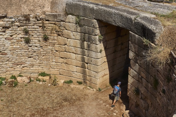 Visitor walks through huge stone gate, Mycenaean domed tomb, archaeological site, UNESCO World