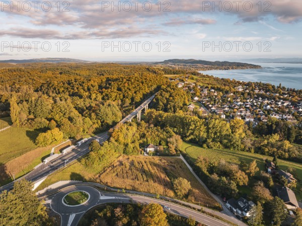 Highway through a forest, with a view of a nearby town and the lake on the horizon under clouds,