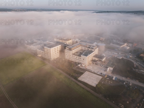 Large industrial buildings surrounded by fields under a thick layer of fog, new hospital health