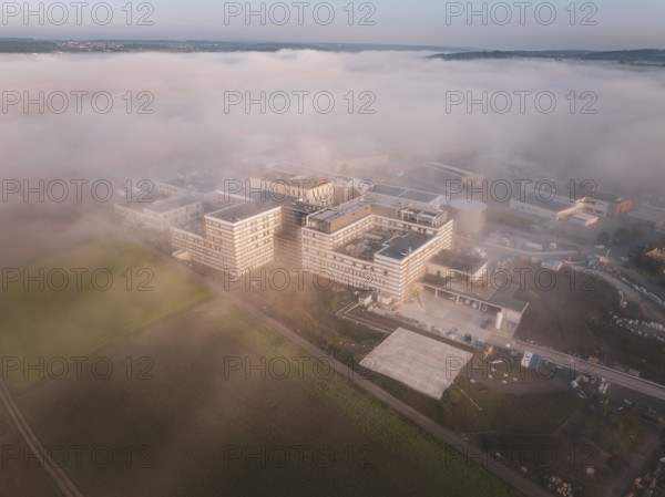 Industrial buildings seen from the air in morning fog, surrounded by natural landscape at dusk, new