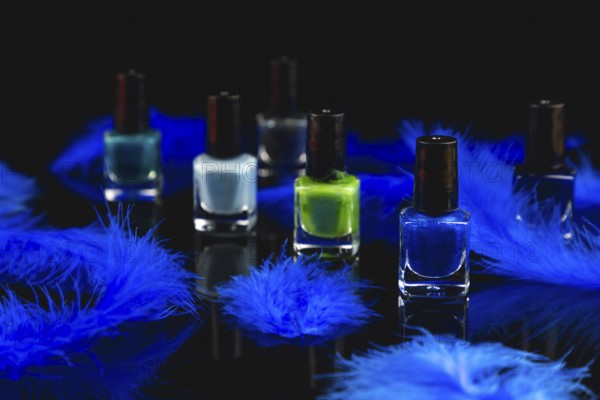 Nail polish bottles in shades of blue and green with blue feathers on a black surface with