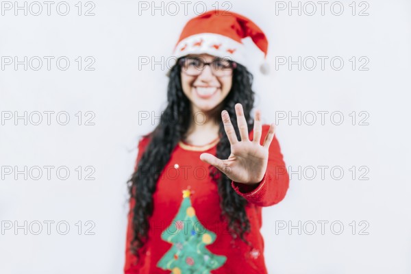 Smiling girl in Christmas sweater counting five. Funny girl in a Christmas hat counting five,