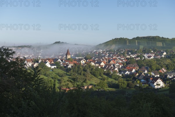 Idyllic village with church surrounded by hills, morning mist and green landscape, Rems Valley,