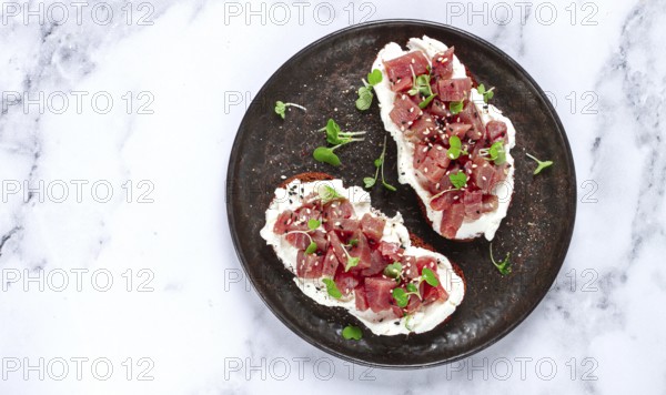 Sandwiches, rye bread with cream cheese, sliced tuna fillet with herbs, breakfast on a black plate,