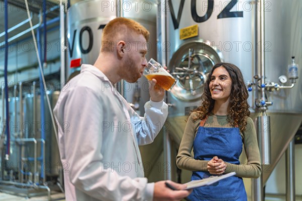 Brewery team performs quality control tasting and discussion beside stainless steel fermenters,