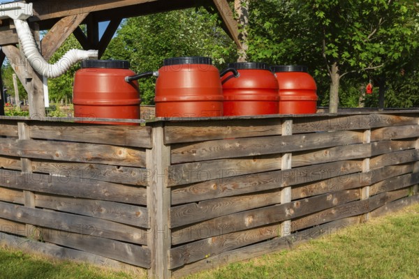 Reddish brown plastic water butts collecting and storing rain water from white plastic downspout in