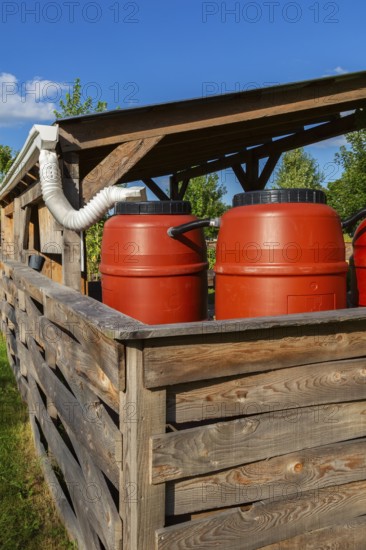 Reddish brown plastic water butts collecting and storing rain water from white plastic downspout in