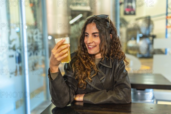 Woman in a leather jacket smiling and savoring a glass of craft beer at a modern brewery bar,