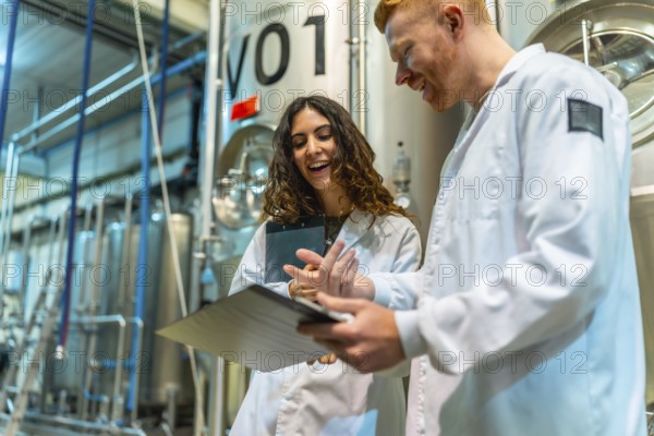 Brewery colleagues smiling and discussing production notes on a clipboard, standing in a beer