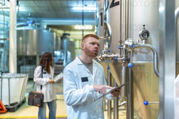 Brewery quality control team inspecting industrial fermentation tanks, a technician monitoring data