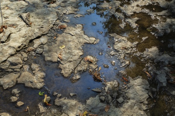 Accidental spilled oil in puddle of water in dried out flat rock river bed due to lack of rainfall
