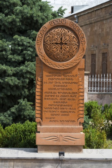 An elaborately engraved stone khachkar with complex ornaments and Armenian characters, surrounded