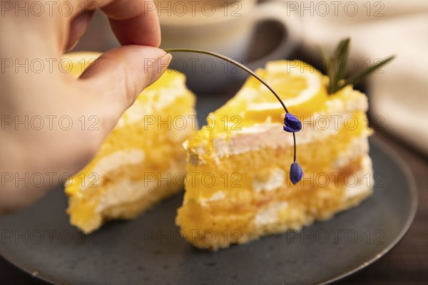Lemon cake with hand on brown wooden background and linen textile, cup of coffee, side view, close