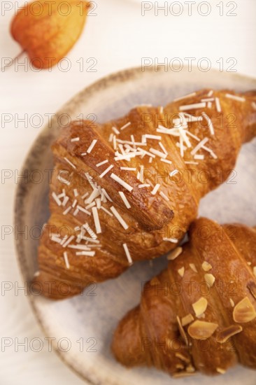 Croissant on blue plate on white wooden background and orange linen textile, cup of coffee, side