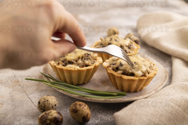 Tartlets with meat and cheese with hand on brown concrete background and linen textile. side view,