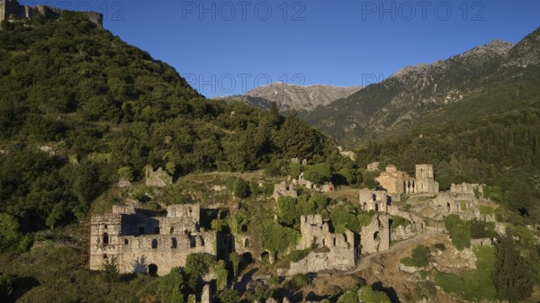 Drone shotRuins and buildings on a hill surrounded by green mountain landscape, including the