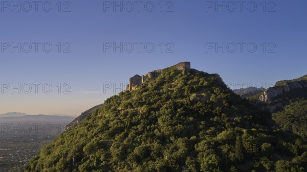 Byzantine castle from the 13th century AD on a green hill in the sunrise, surrounded by forest,