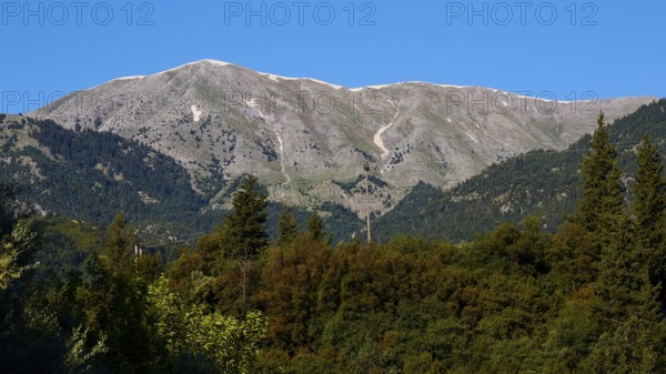 A high mountain rises above dense trees under a bright blue sky, Mystras, Mistra, UNESCO World