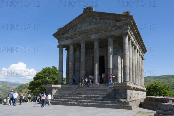 Ancient temple with visitors, surrounded by green nature and stone structures, Greek-Roman Temple