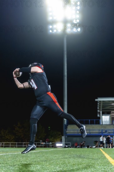 American football player in black and orange uniform catching an airborne football on a green turf