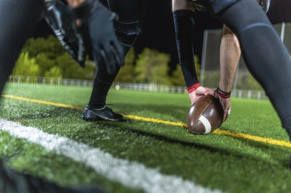 American football player is positioning the leather ball on the marked artificial turf field during