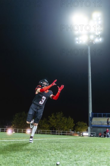American football player in uniform with a number 3 catching a ball on a lit artificial turf field