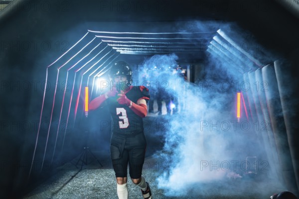 American football player in uniform and helmet emerging from a stadium tunnel filled with smoke and