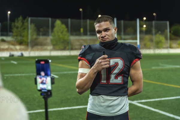 American football player in uniform number 12, standing on a green sports field at night, holding a