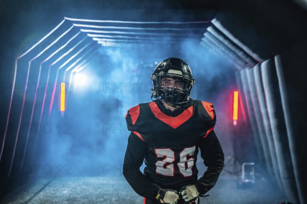 American football player in uniform and helmet emerges from a fog filled stadium tunnel into