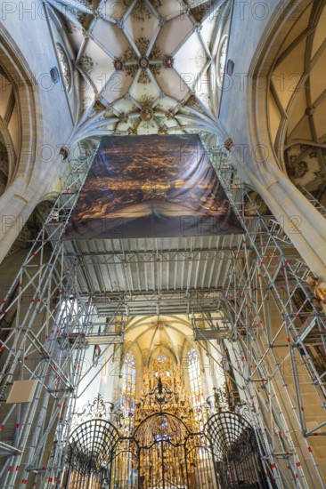 Magnificent church interior with scaffolding and golden decorations, covered by a painted banner,