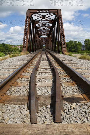 Railroad tracks leading to old rusted Terrebonne Pratt truss railroad bridge over Des Mille-Iles