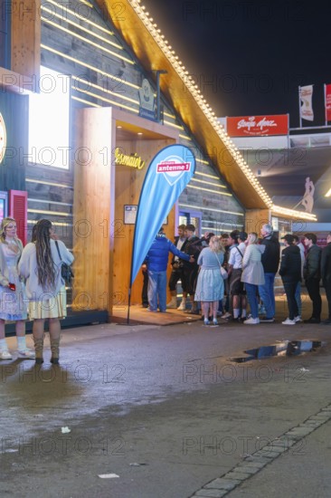 People standing in front of an illuminated marquee at night while waiting for admission,