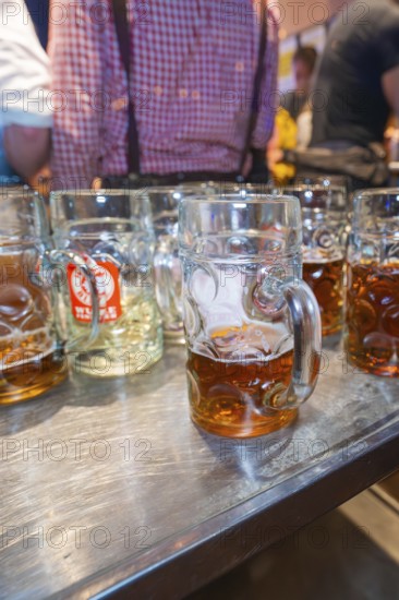 Large glass mugs of beer on a wooden table surface in a lively festival setting, Cannstatter Wasen