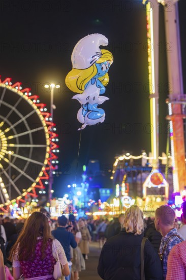 View of a Smurf balloon floating between a crowd at a funfair, with Ferris wheel in the background,