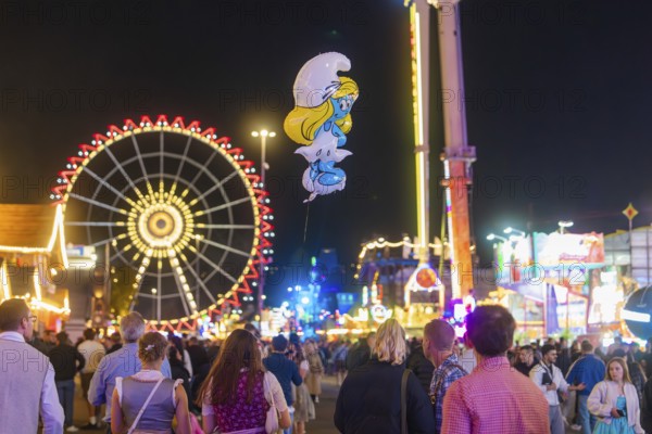 People enjoying the hustle and bustle of a fairground at night with a large Ferris wheel in the