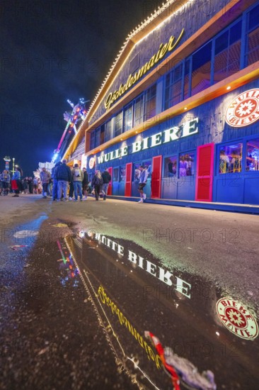 Reflection of the colourful lights of a beer hall on a wet street at night, Cannstatter Wasen folk